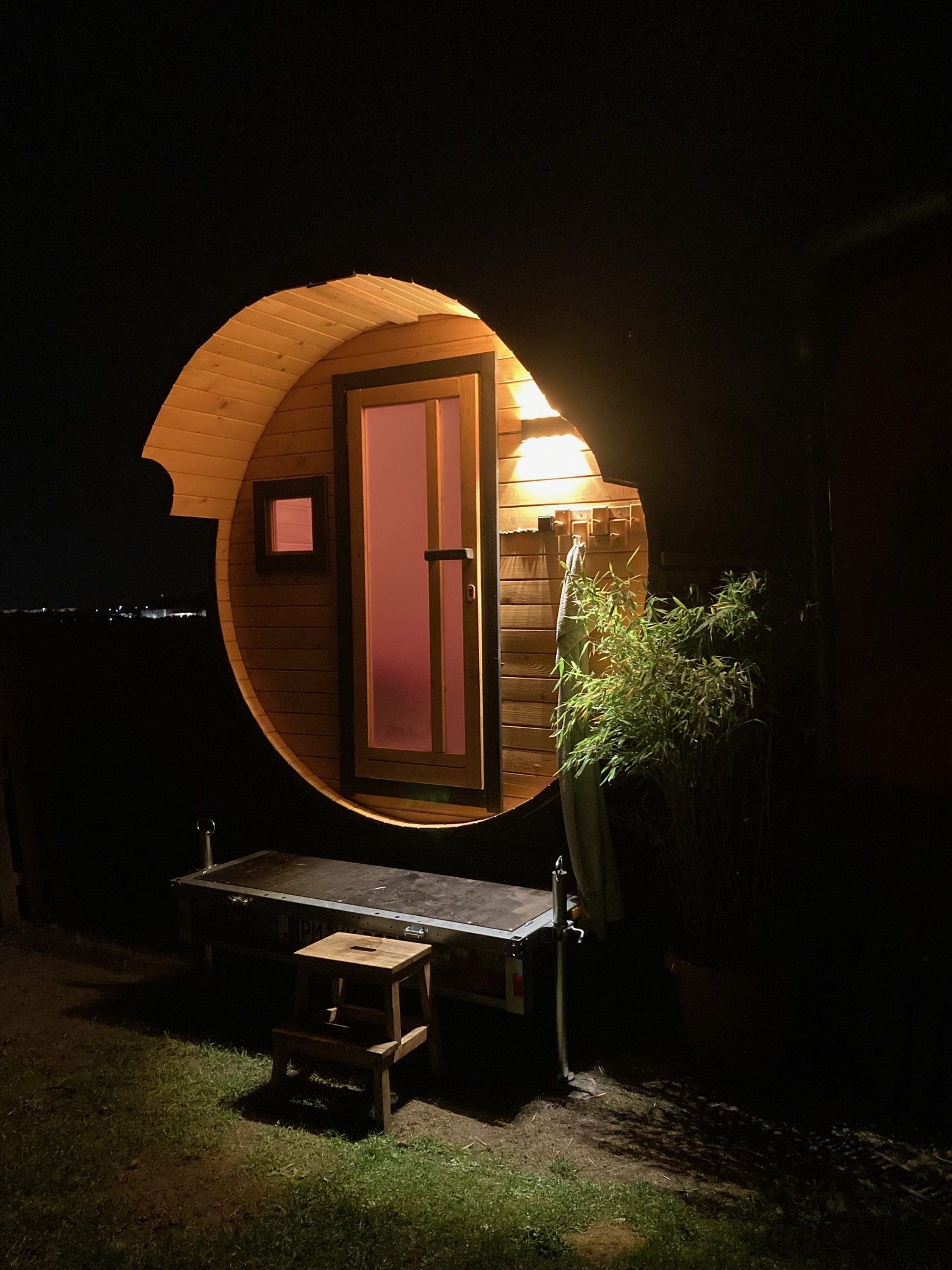 Mobile Fasssauna am Abend mit beleuchtetem Eingang, Holzbank und Stufe davor